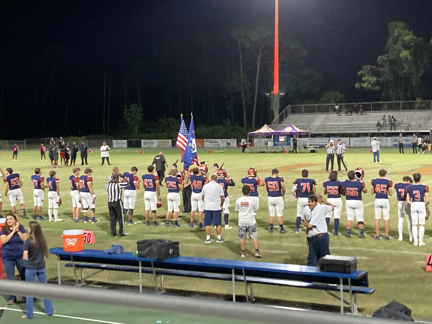 Players line the sideline for the national anthem before a Friday night high school football game.