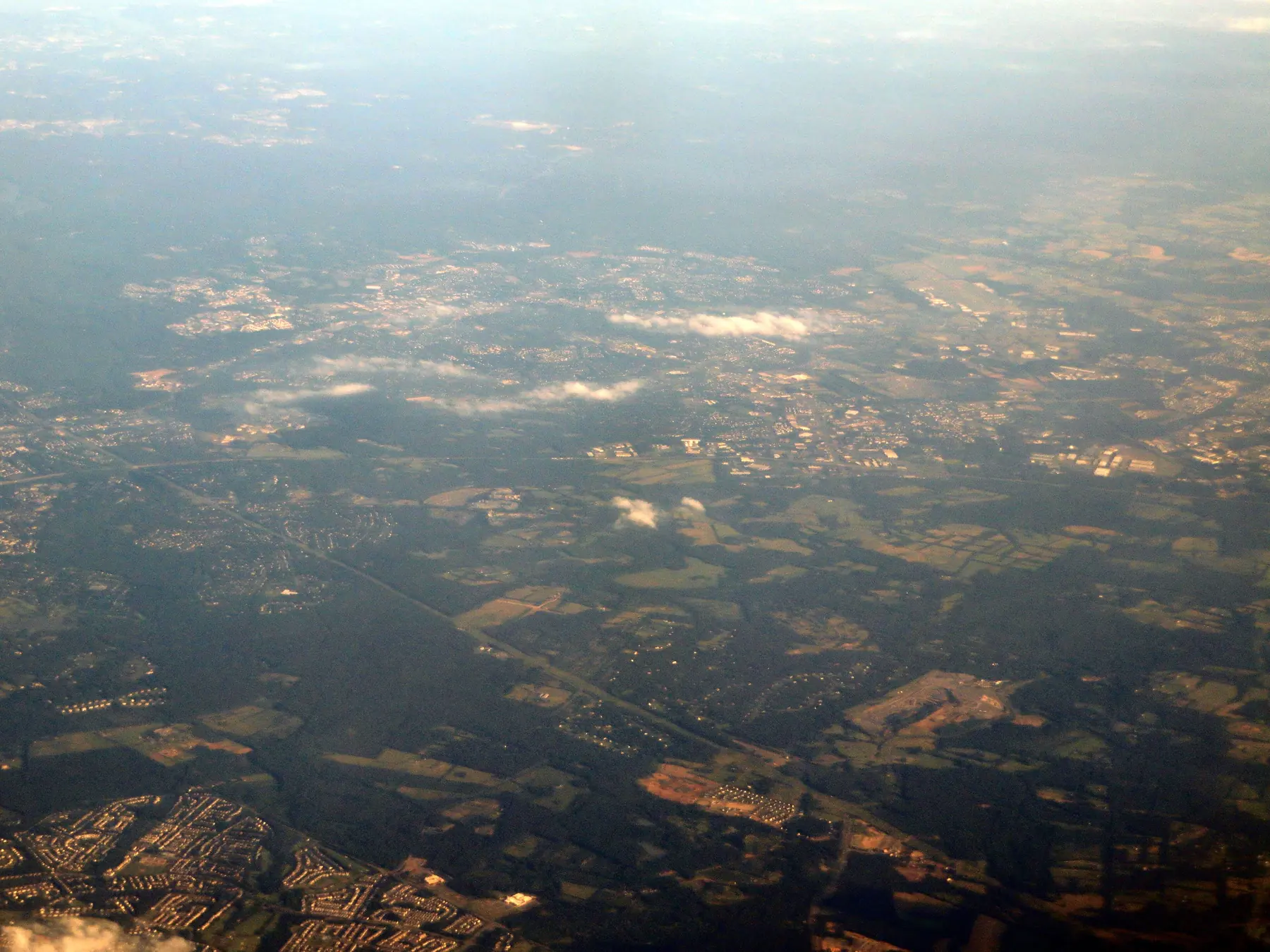 An aerial view over the city of Manassas and neighboring Manassas Park, with homes, roads and tree cover below.