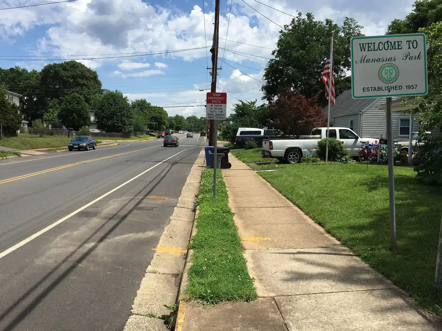 The "Welcome to Manassas Park" sign on Manassas Drive (Route 213) at the city line, with houses along the street.